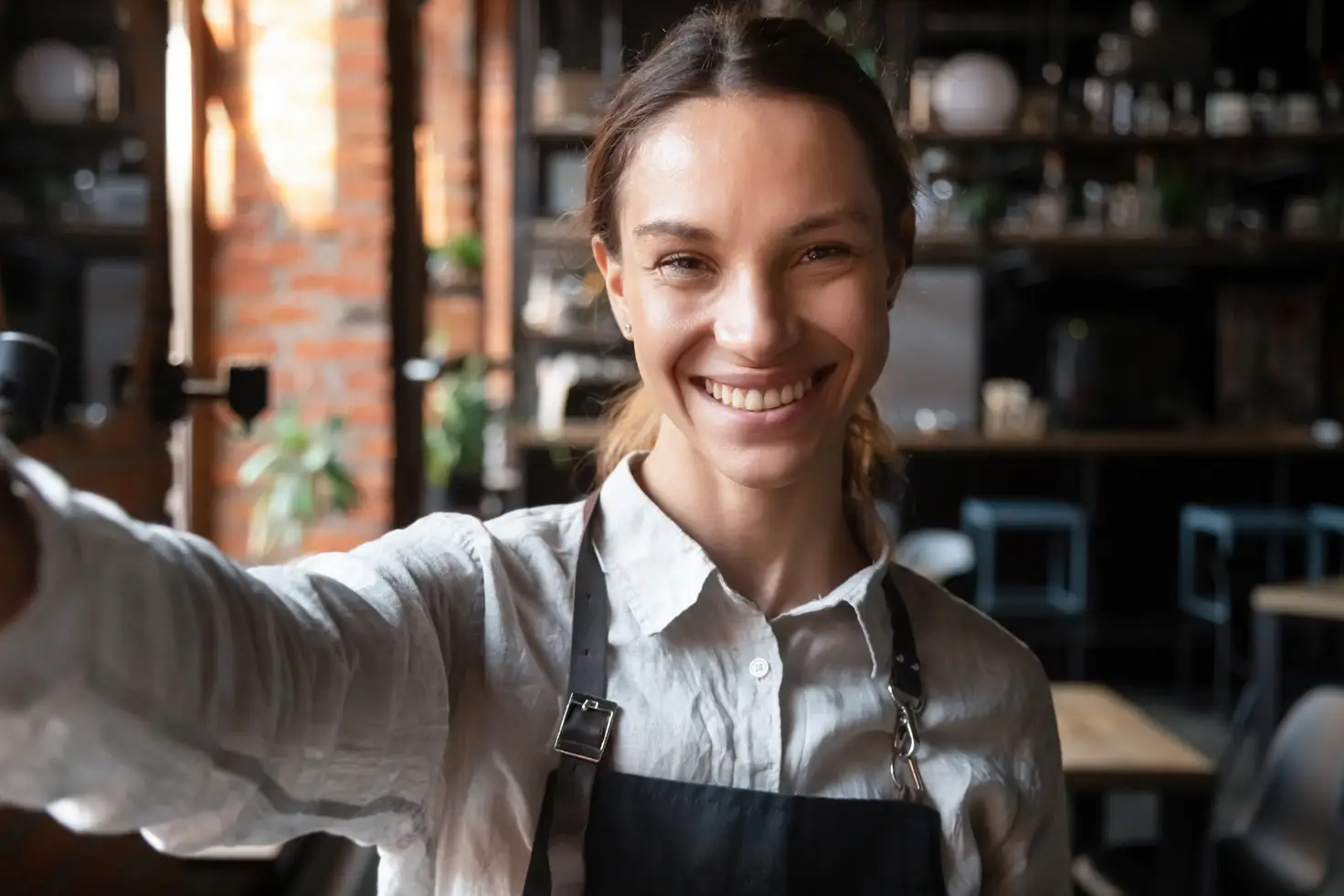 Woman,Wearing,Apron,In,Cafe,Holding,Webcam,Look,At,Camera